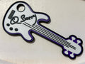 A 3D printed custom guitar-shaped figure keepsake featuring a white body with purple trim, black outlines, and a black script signature reading 'Q Barry' on the headstock area, shown on a light beige background. Custom made by NickNacks for the Bass for Berry fundraiser benefiting Quintin Berry.